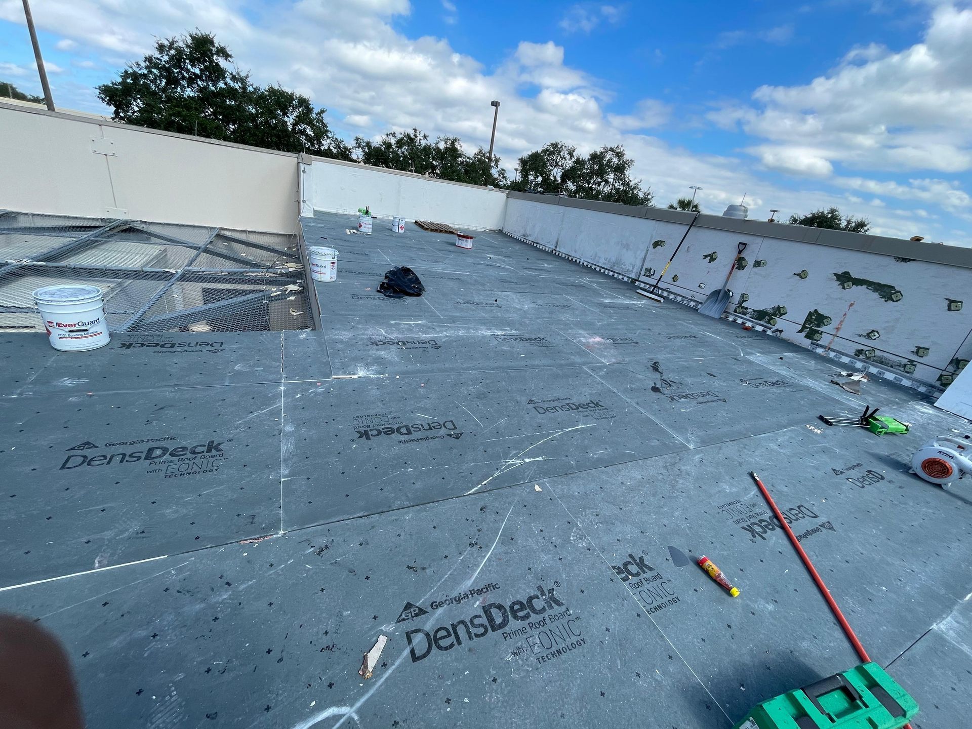 Roofing construction site with gray DenckDeck, tools, and materials under a blue sky.