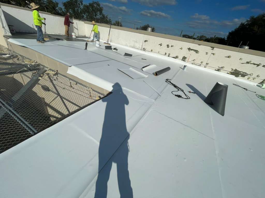 Workers installing a white roof membrane on a building. Blue sky overhead.