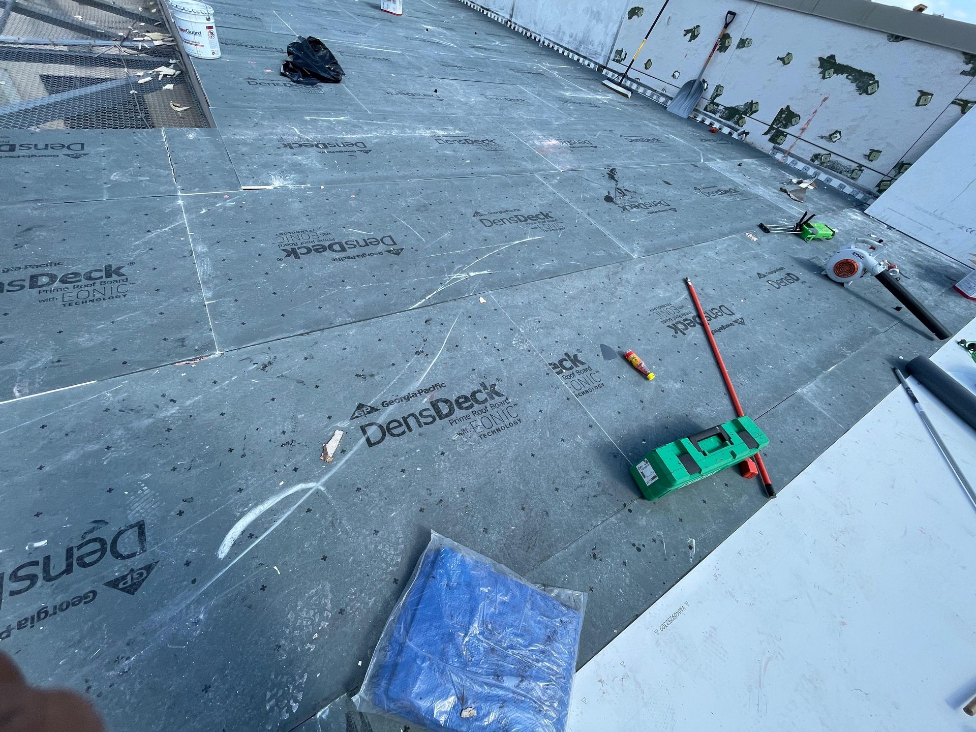 Construction site with grey sheathing, tools, and a blue tarp on a roof.