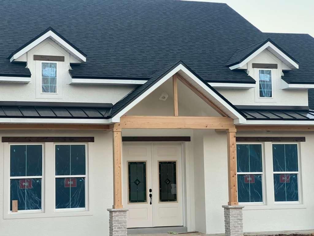 White stucco house with black roof, wooden accents, and dormer windows.