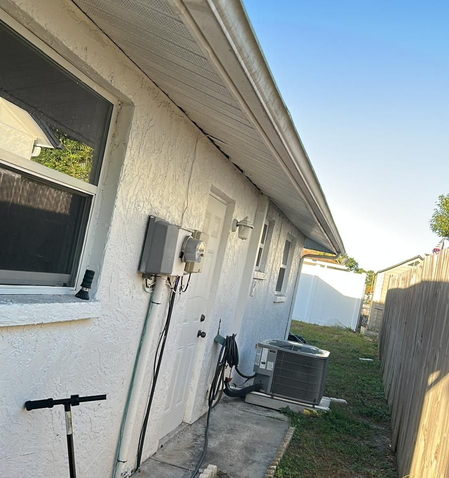Exterior wall of a white house with windows, door, electrical box, and AC unit.