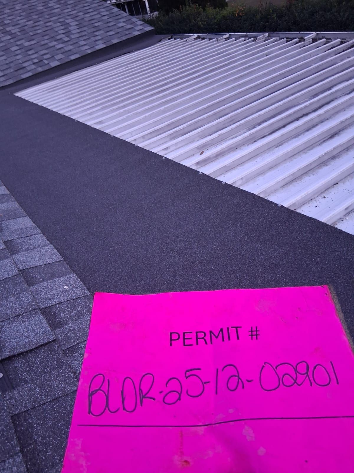 Pink permit slip on roof with metal and asphalt shingles. Permit # is BLDR-23-12-02801.