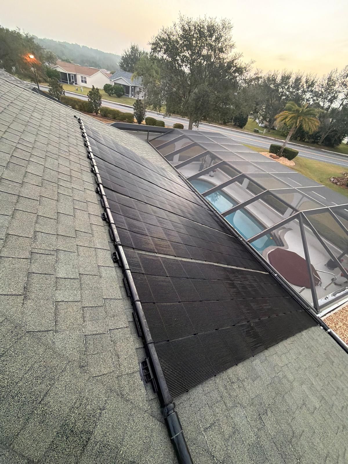 Solar panels installed on a sloped roof next to a screened-in pool enclosure.