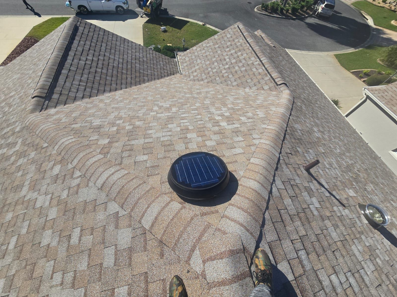 Overhead view of a house roof with brown shingles, and a solar-powered vent fan.