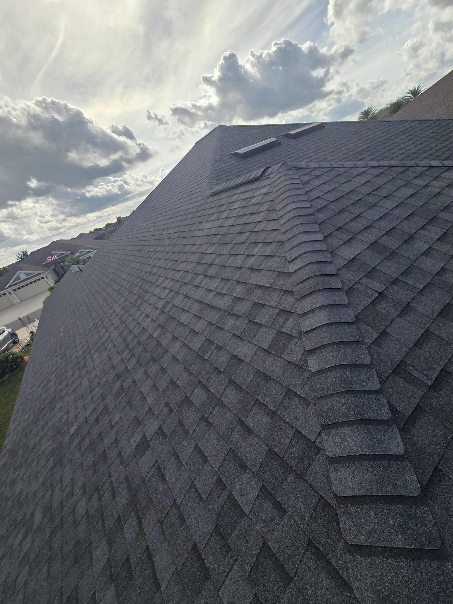 Dark asphalt shingle roof on a cloudy day.
