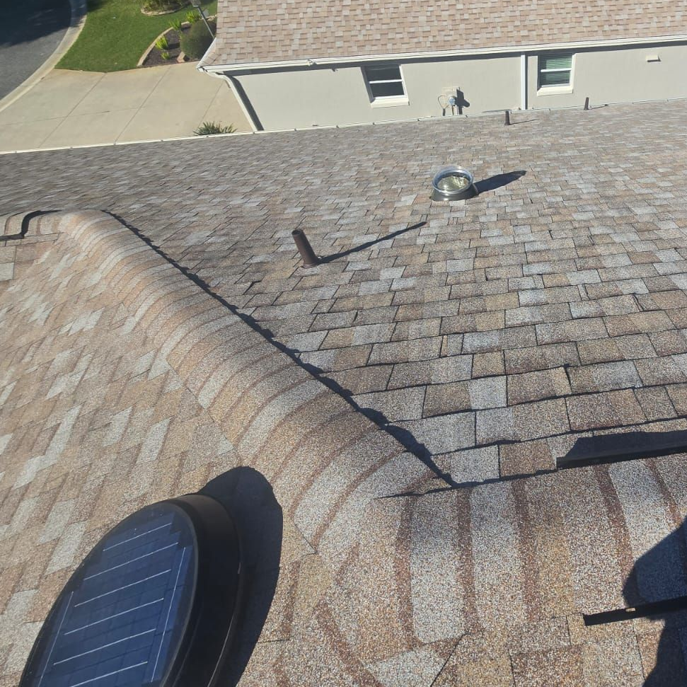 Brown asphalt shingle roof with solar vent and chimney, angled perspective, sunny day.