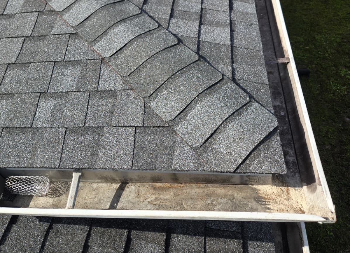 Close-up of gray asphalt roof shingles meeting a white metal gutter and roof edge.