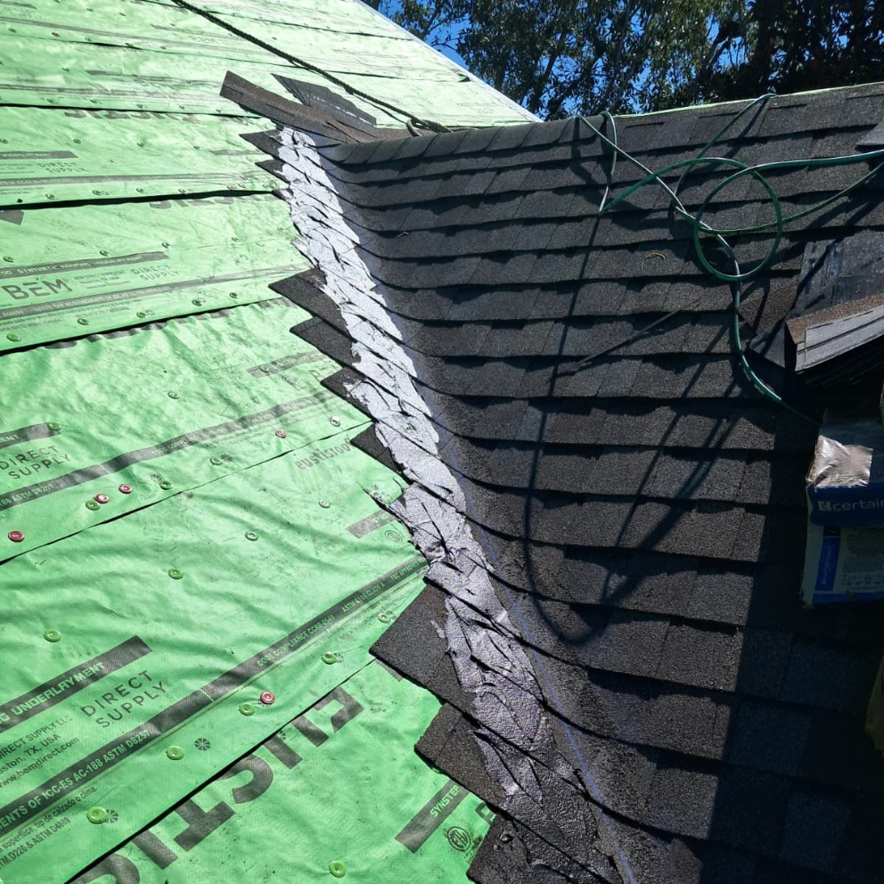 Roof being shingled; close-up view showing installed shingles, underlayment, and exposed roof edge.