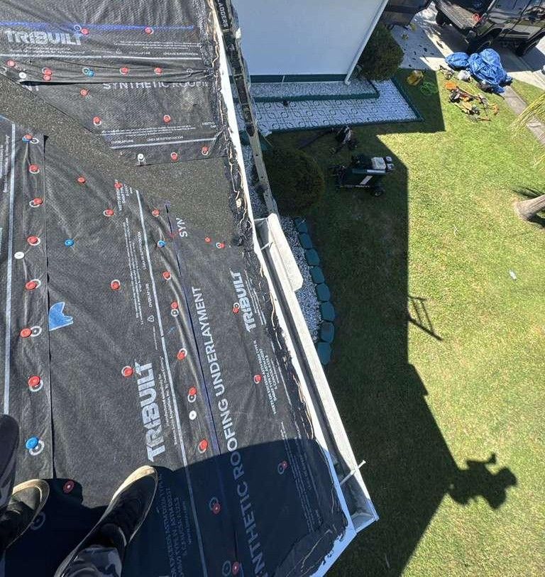 Roofer installing synthetic roofing underlayment on a house roof. Green grass and yard below.