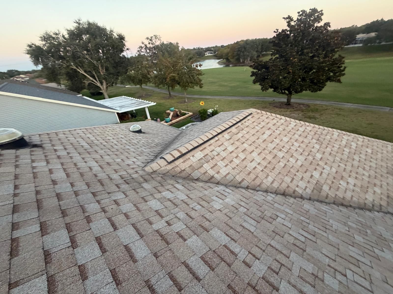 View from a roof of a house, overlooking a golf course with trees and a lake at dusk.