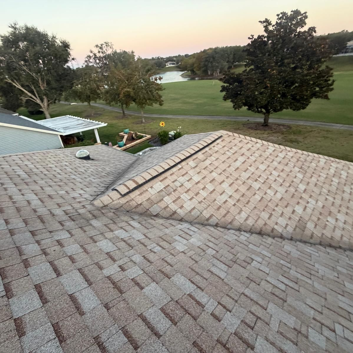 Overhead view of a roof with light brown shingles, overlooking a green golf course and trees.