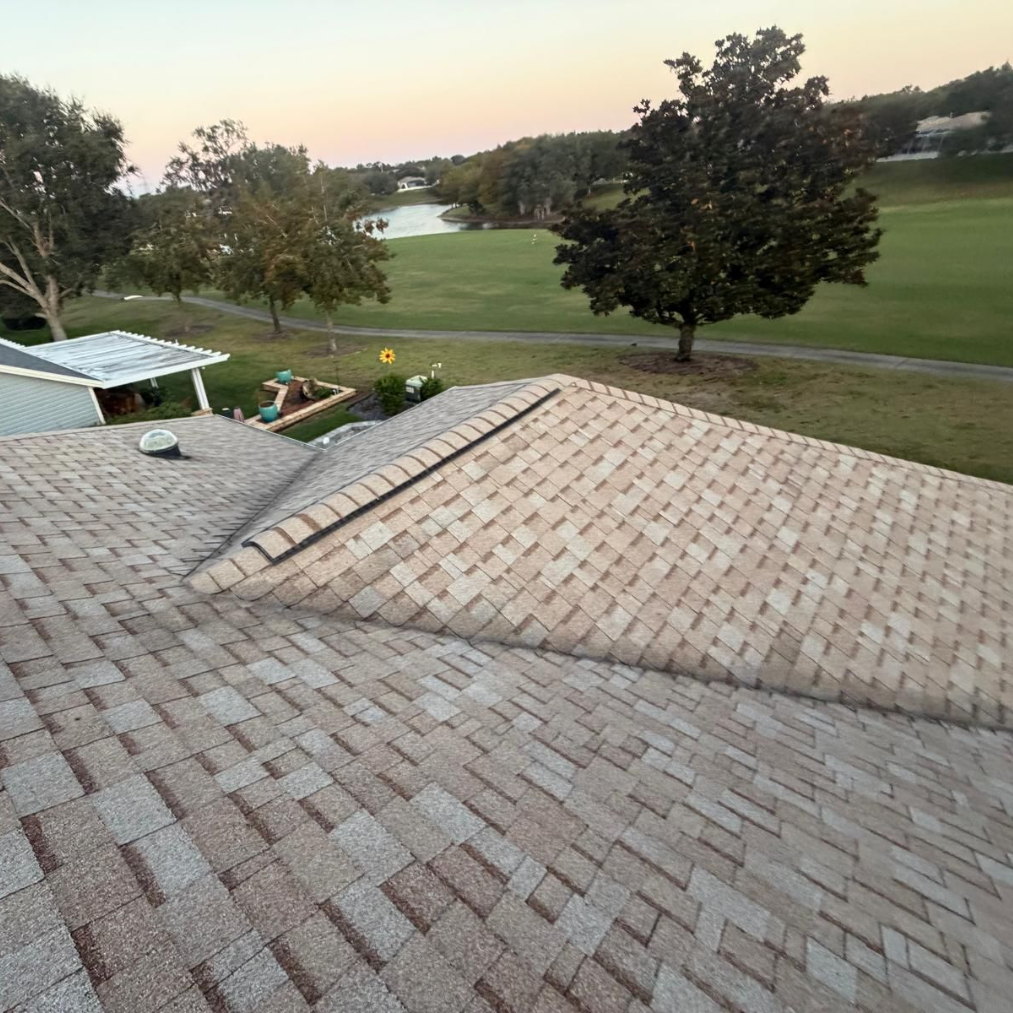 Shingled roof of a house with a golf course and lake in the background under an overcast sky.