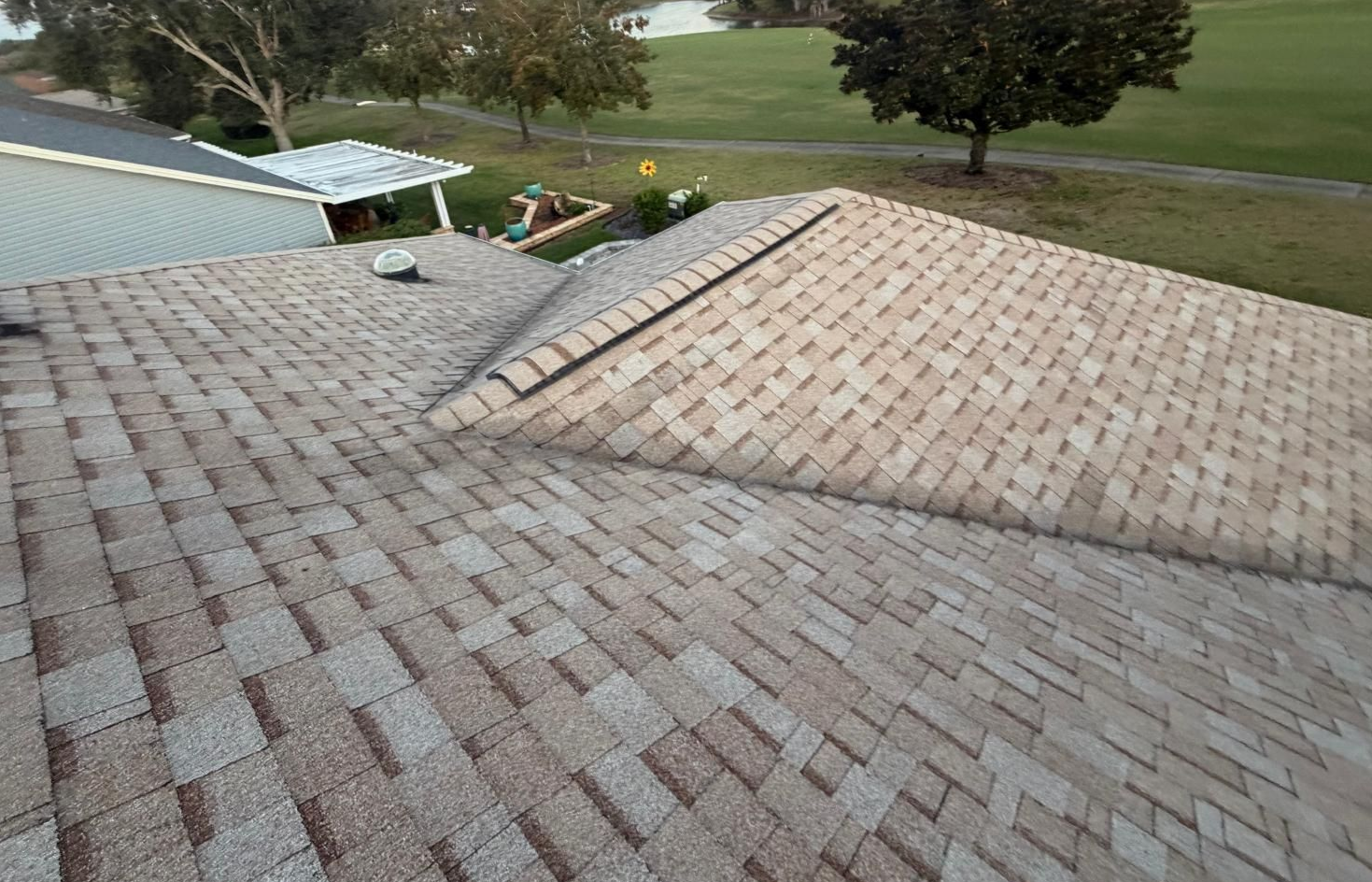 View of a residential roof with overlapping brown and tan shingles, near a tree and green lawn.