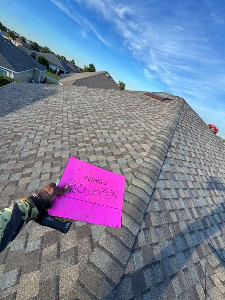 Hand holding pink paper on a shingled roof under a blue sky.