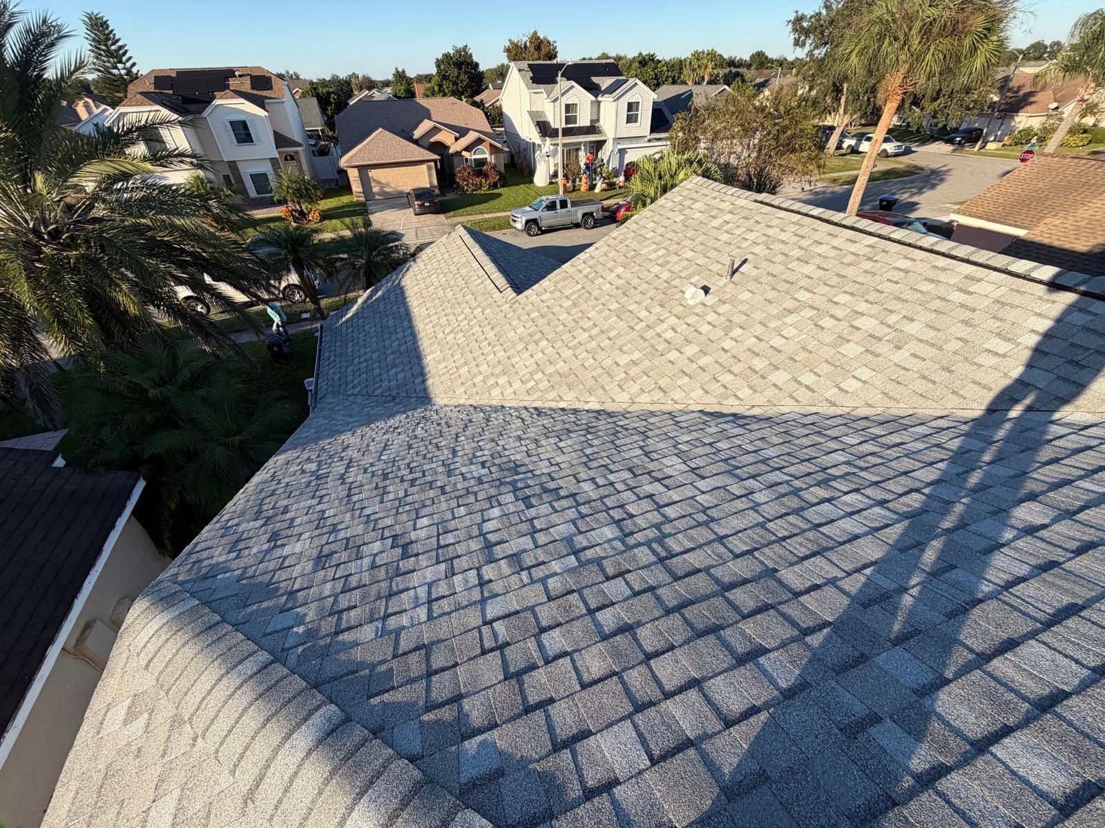 Overhead view of a gray asphalt shingle roof on a residential home with surrounding homes and trees.
