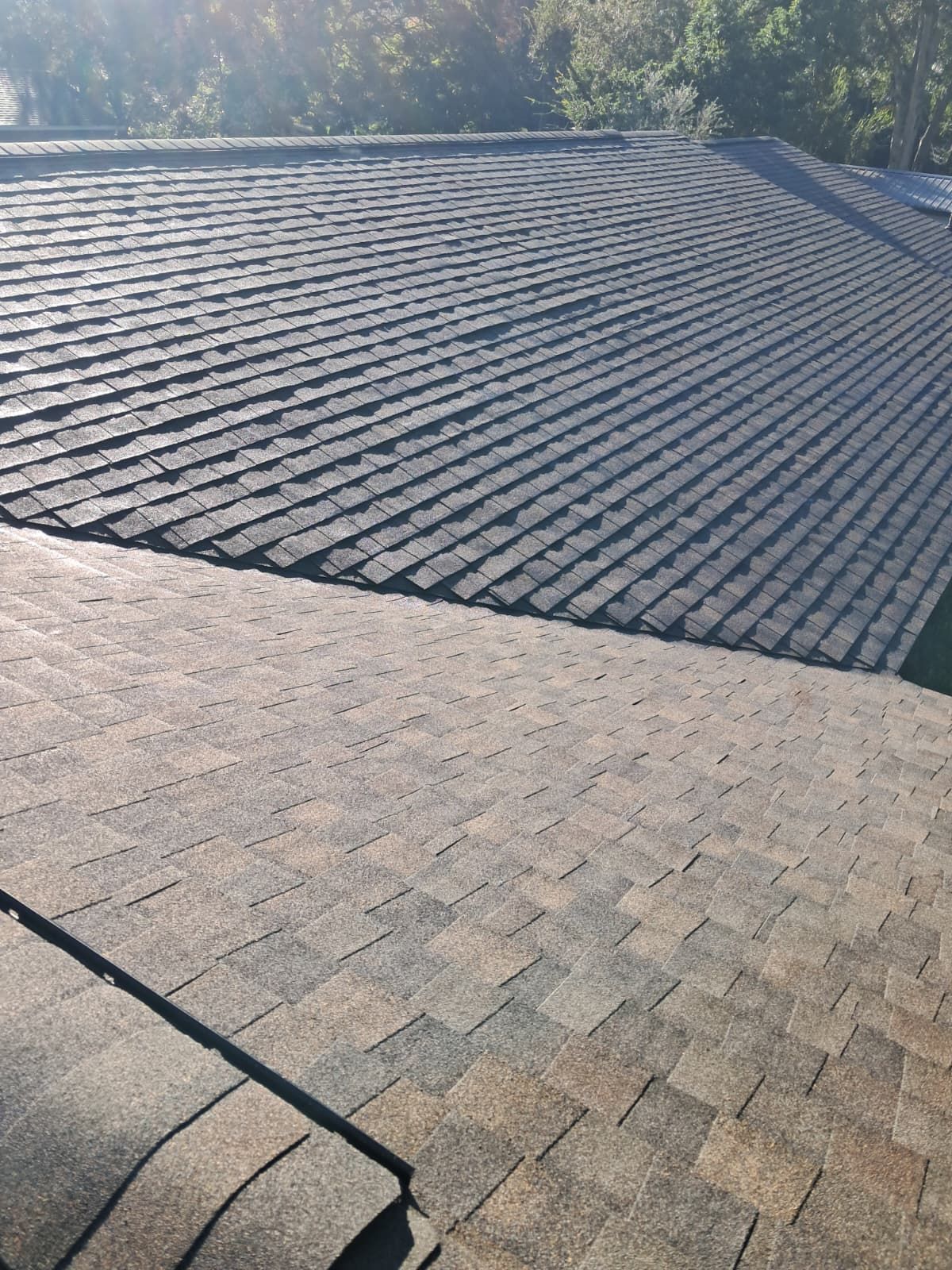 Overhead view of two sections of asphalt shingle roofing; one is dark gray, the other is brown with darker shades.
