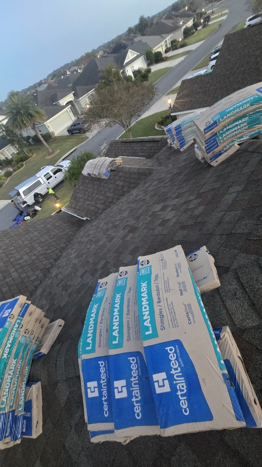 Roof with stacks of blue and white shingle bundles, overlooking a residential street.