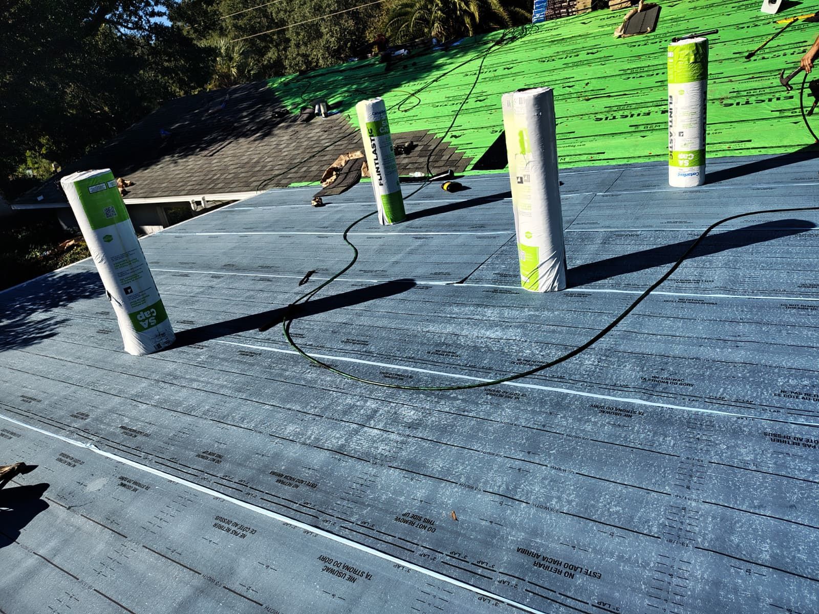 Roofing work: rolls of waterproof material on a dark grey roof, with green roofing in the background.