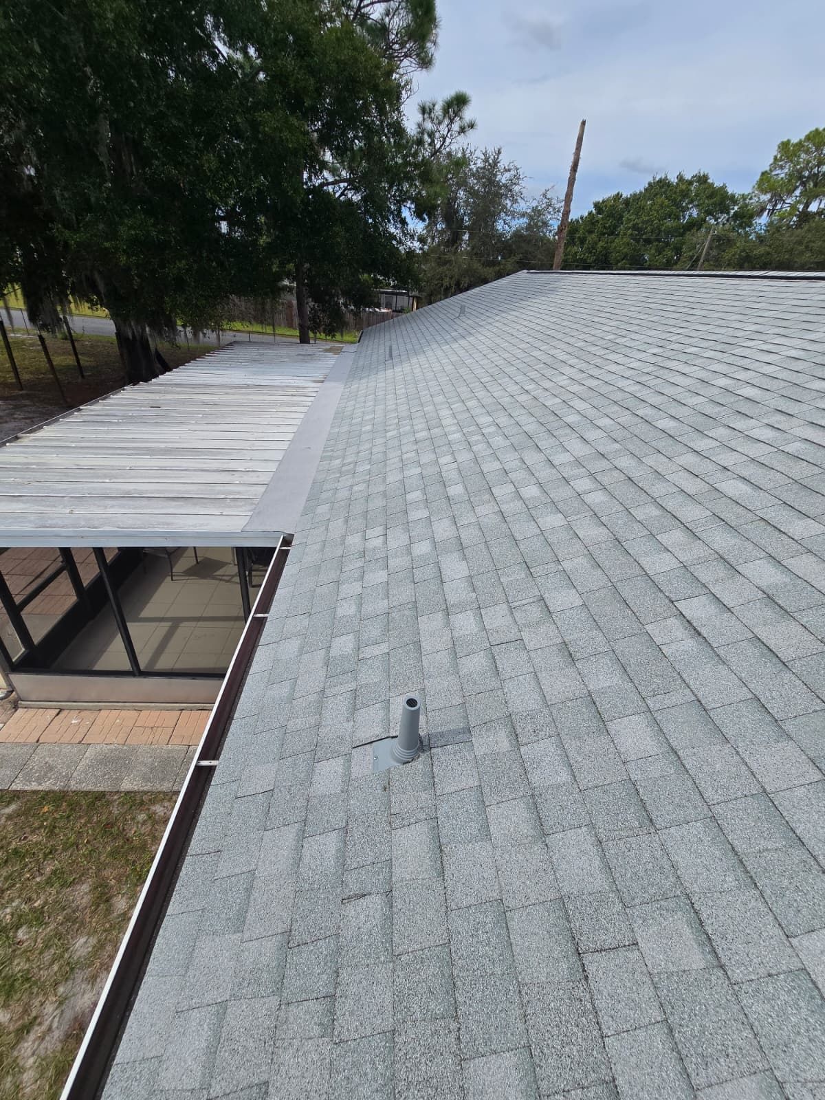 Gray shingle roof, angled view. A vent pipe is visible. The roof sits over a sunroom and lawn.