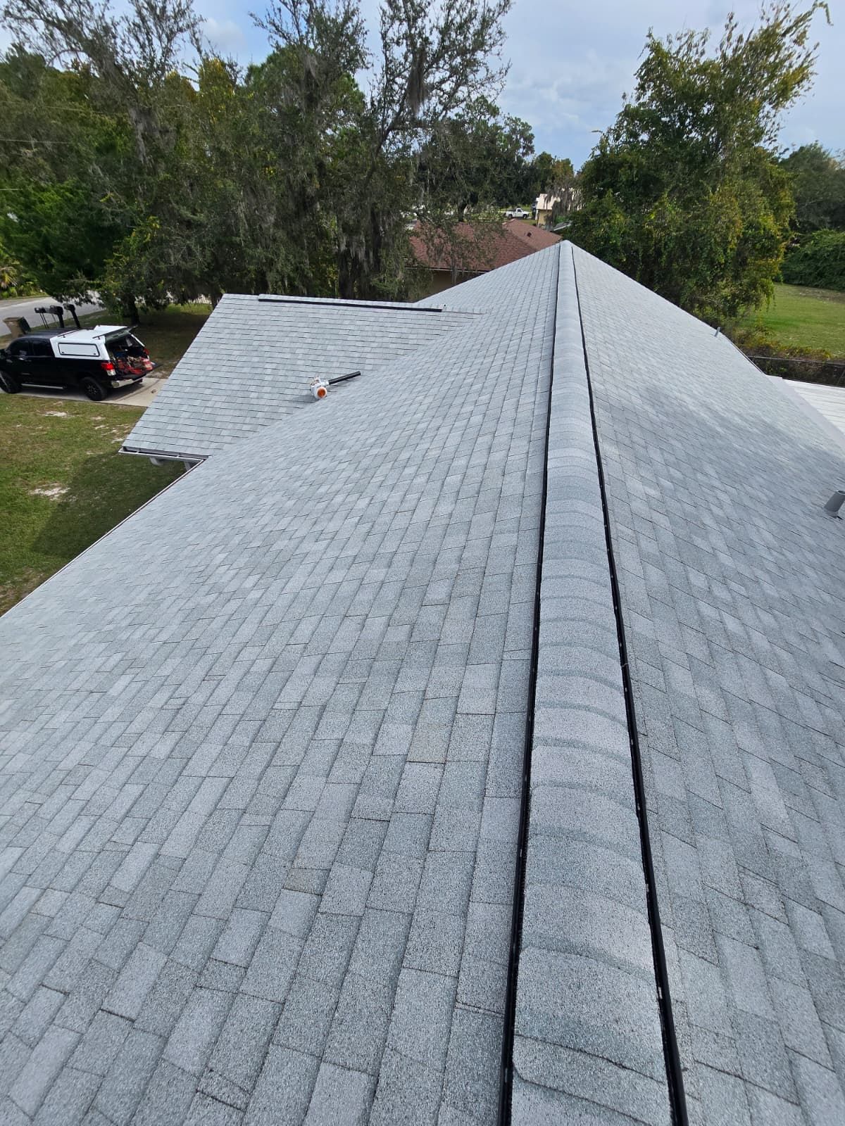 Gray shingle roof, aerial view. Black strip down the center. Green trees and lawn in the background.