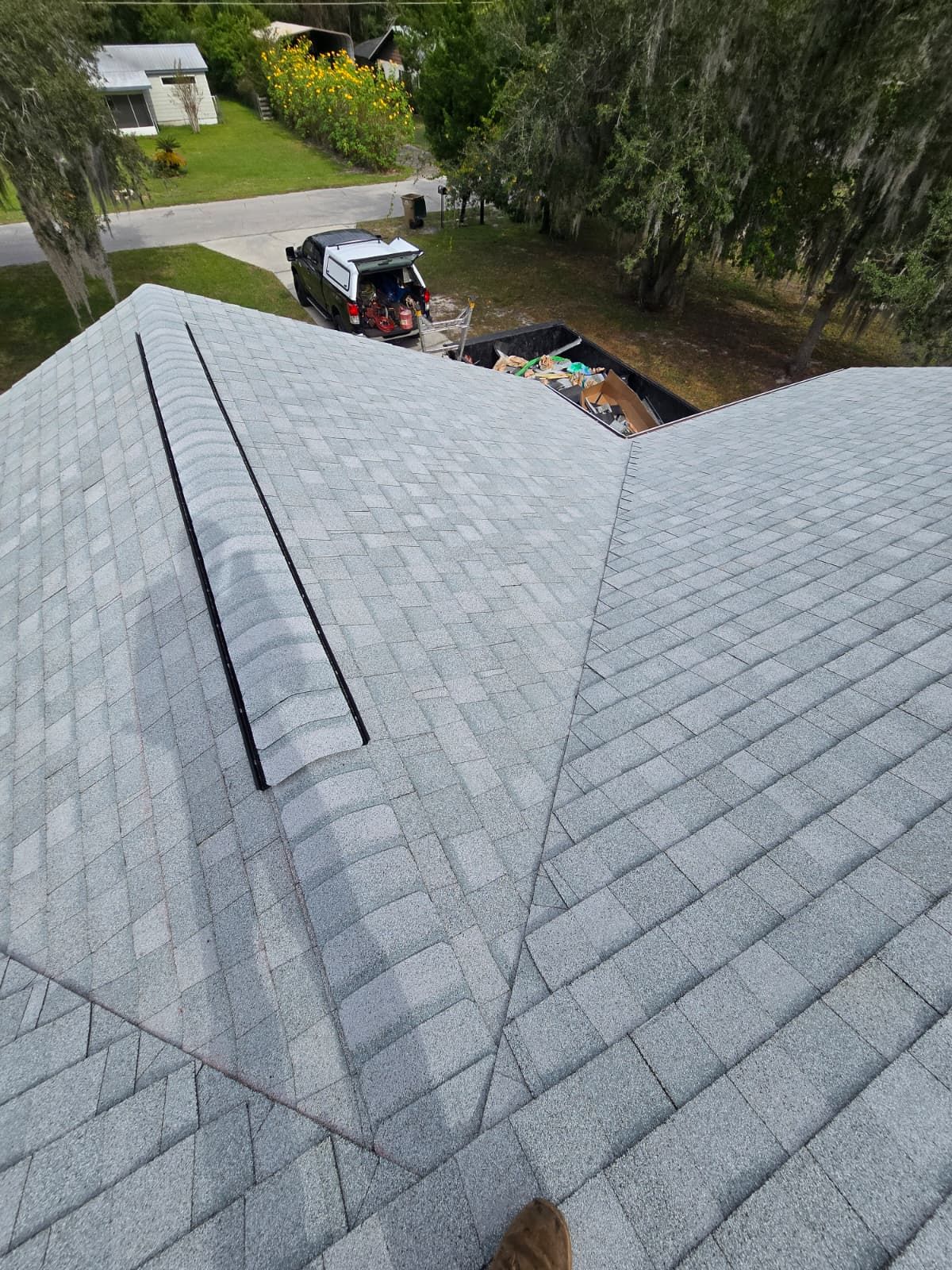 Overhead view of a gray shingled roof with a dark vent, in a suburban setting.