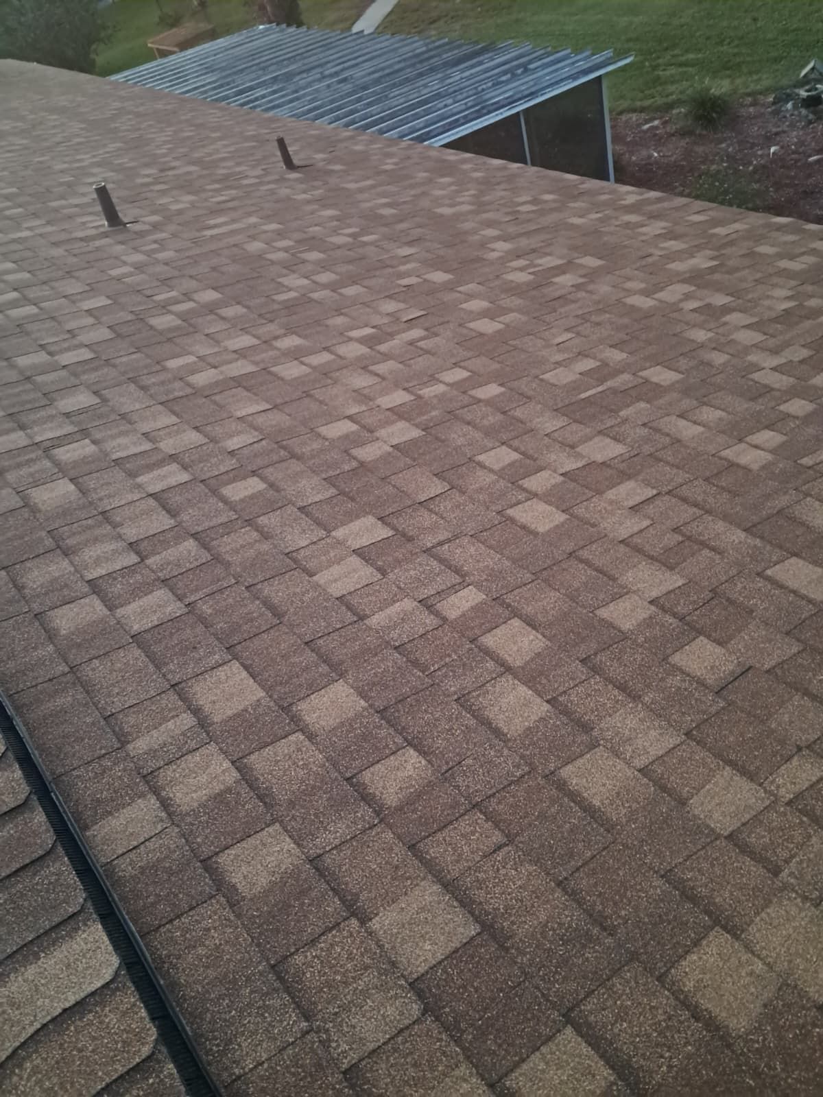 Overhead view of a brown and tan shingle roof with vents; a small, metal roof is in the background.