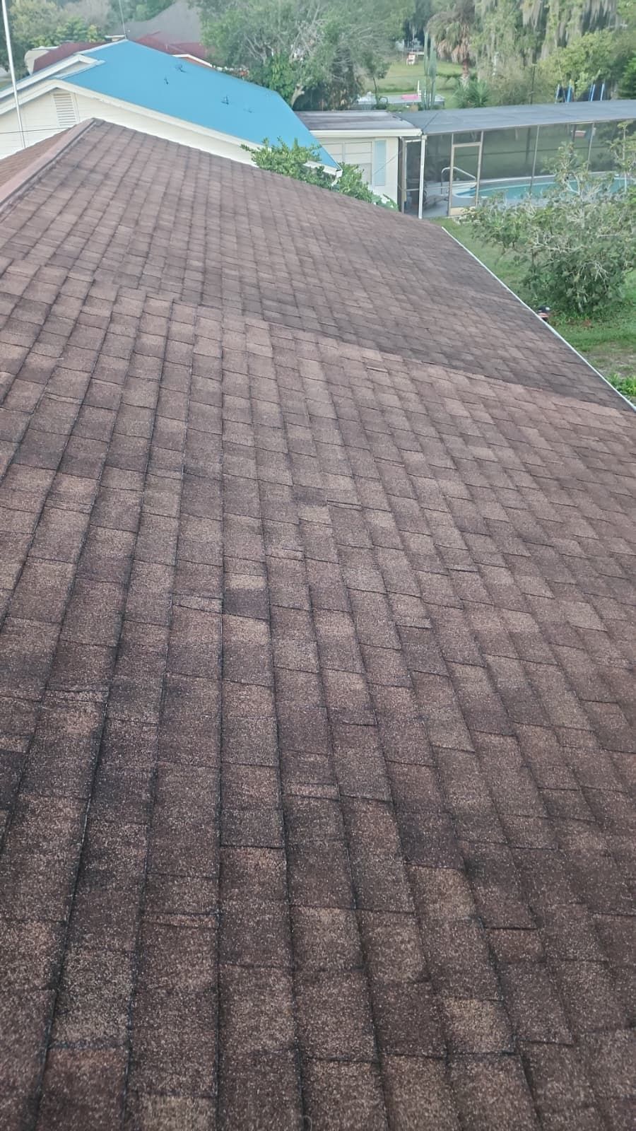 Brown asphalt shingle roof with visible wear and tear, covering a house, trees in the background.
