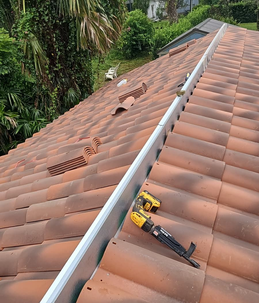 A person installing a metal flashing along the edge of a tiled roof; tools are present.