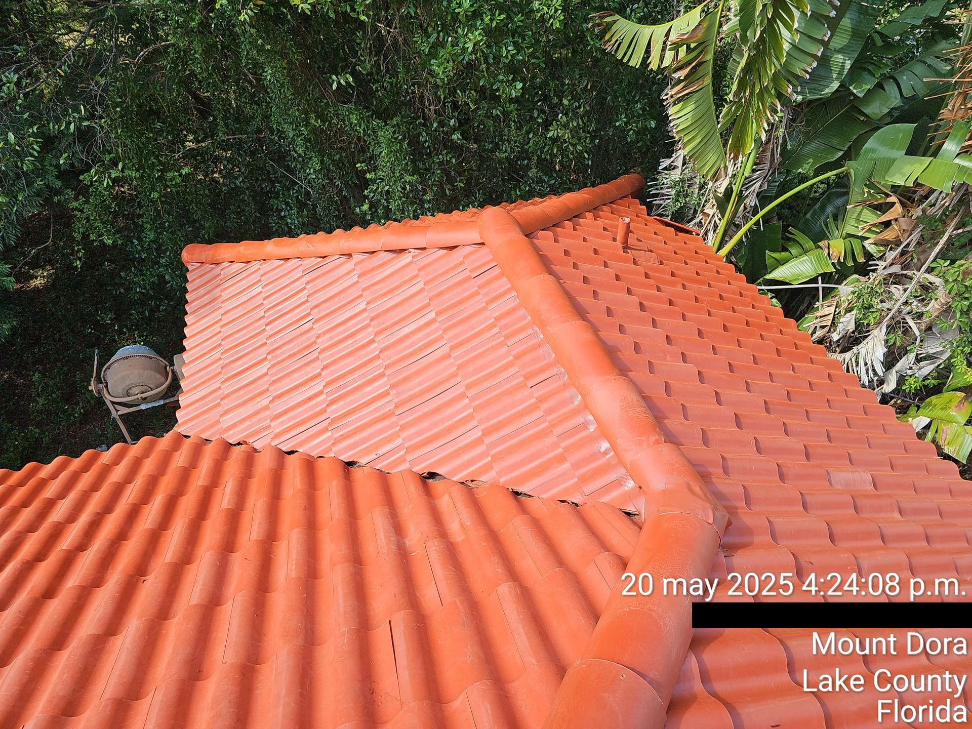 Orange tile roof with a downspout, surrounded by green trees in Mount Dora, Florida.