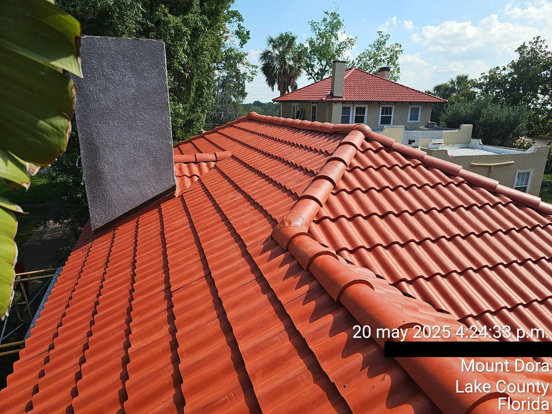 Red tile roof with a chimney, trees, and buildings visible in the background.