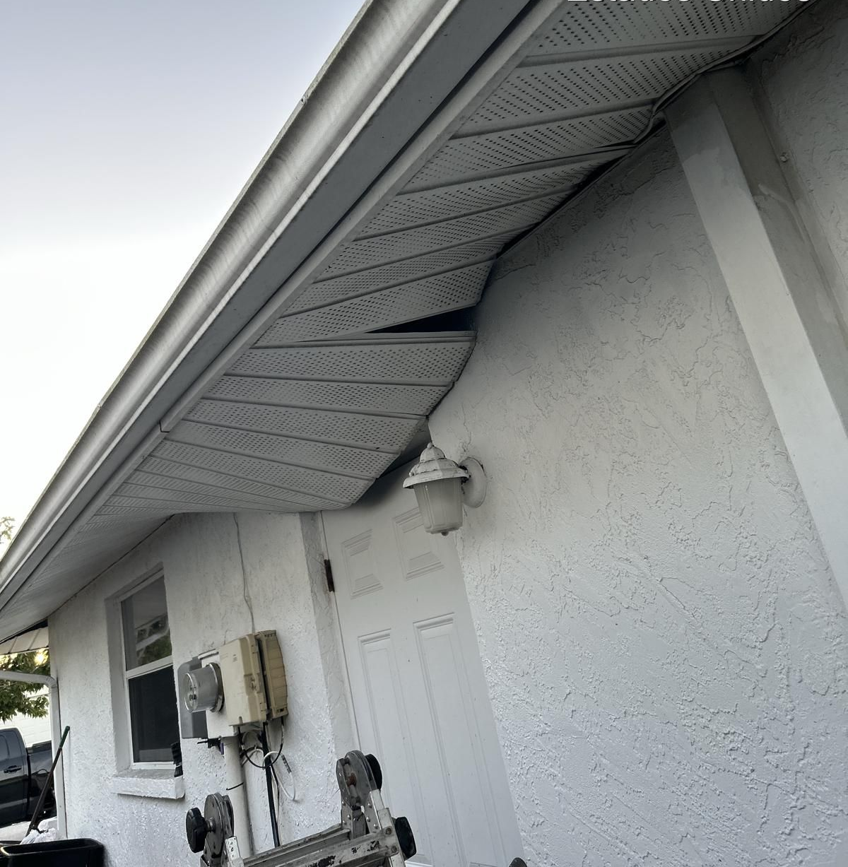White building with damaged soffit and siding, and a security light.