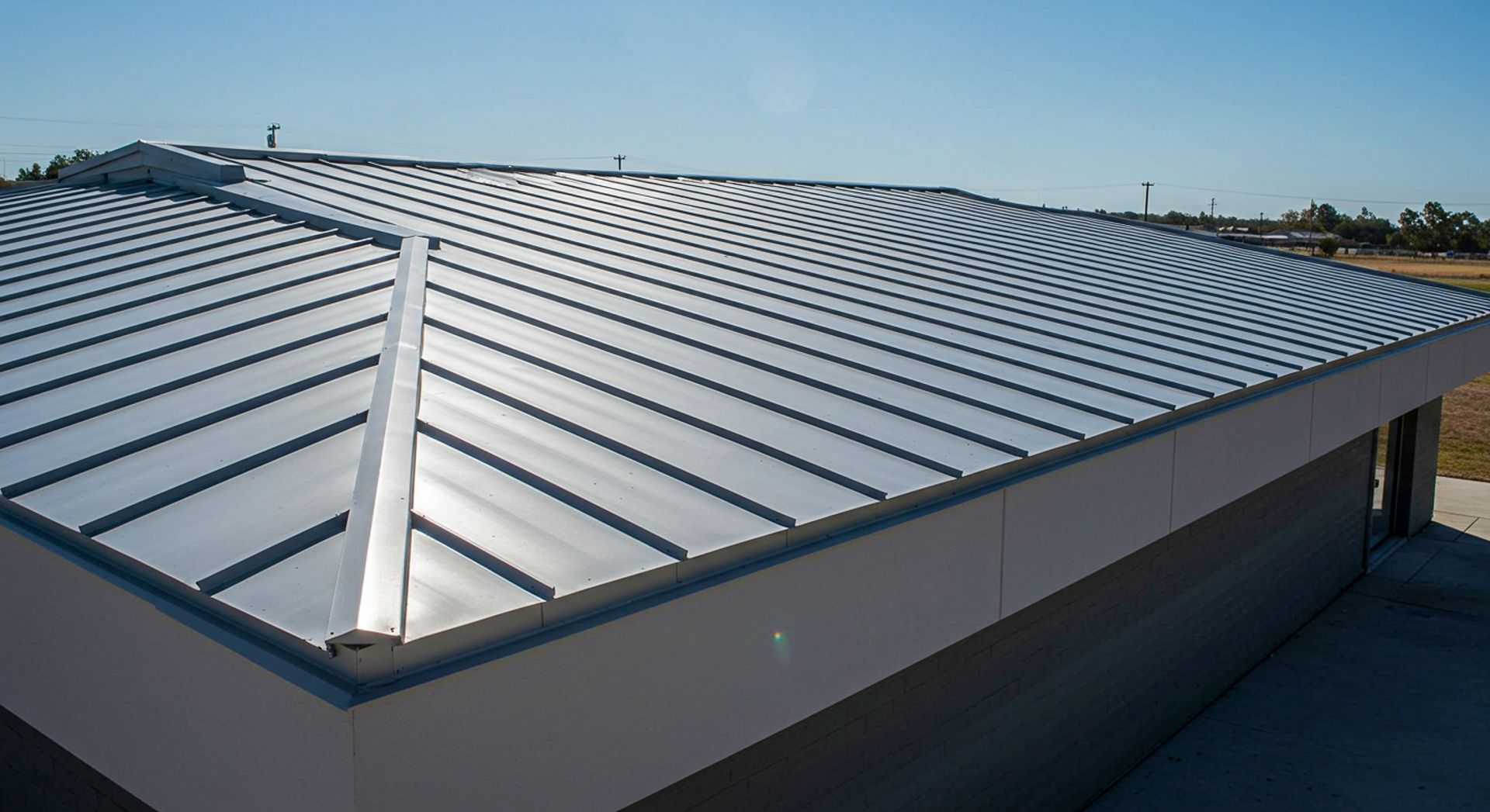 Silver metal roof on a modern building, reflecting sunlight against a clear blue sky.
