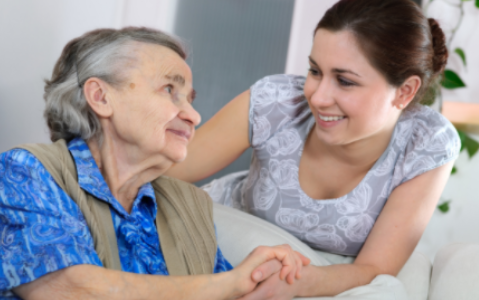 Caregiver smiling and holding hands with an elderly person on a couch