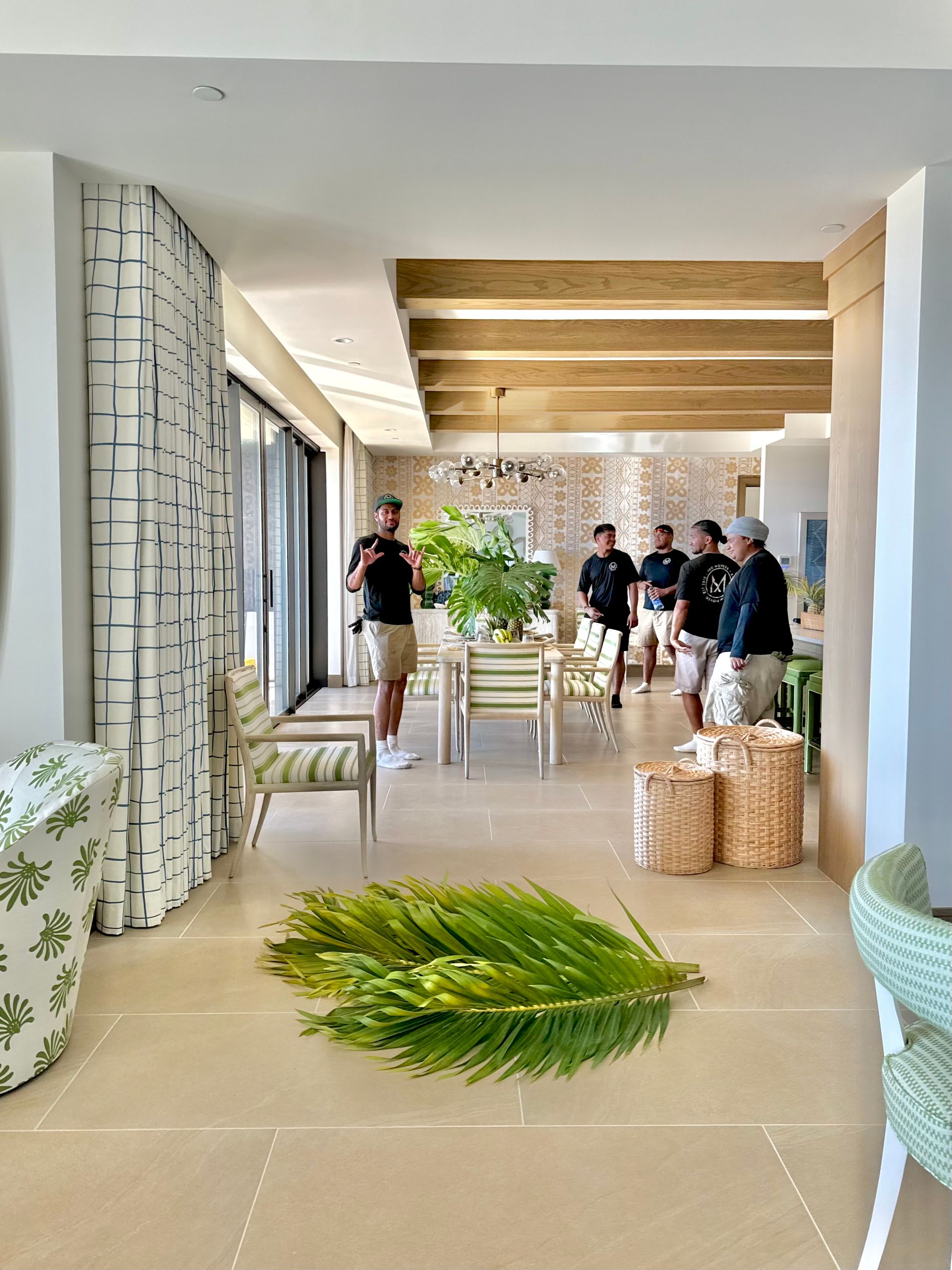 A group of people are standing in a living room with a palm leaf on the floor.
