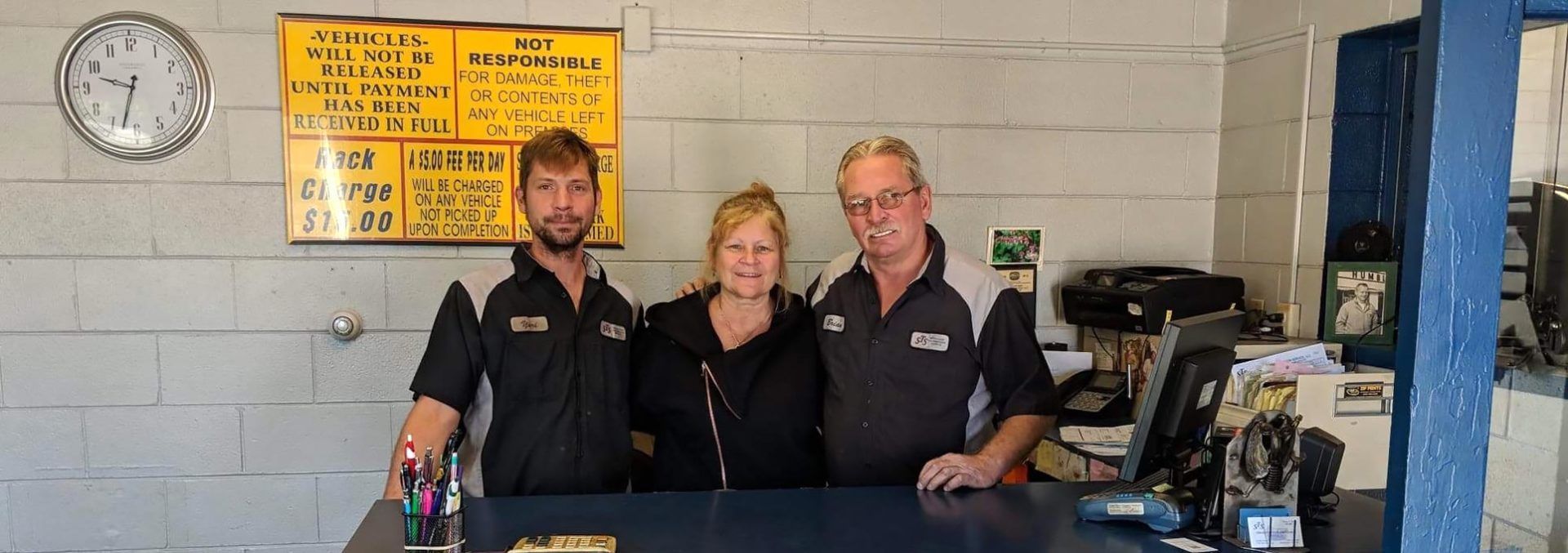 Three people in black shirts standing behind a counter in a workshop or service area