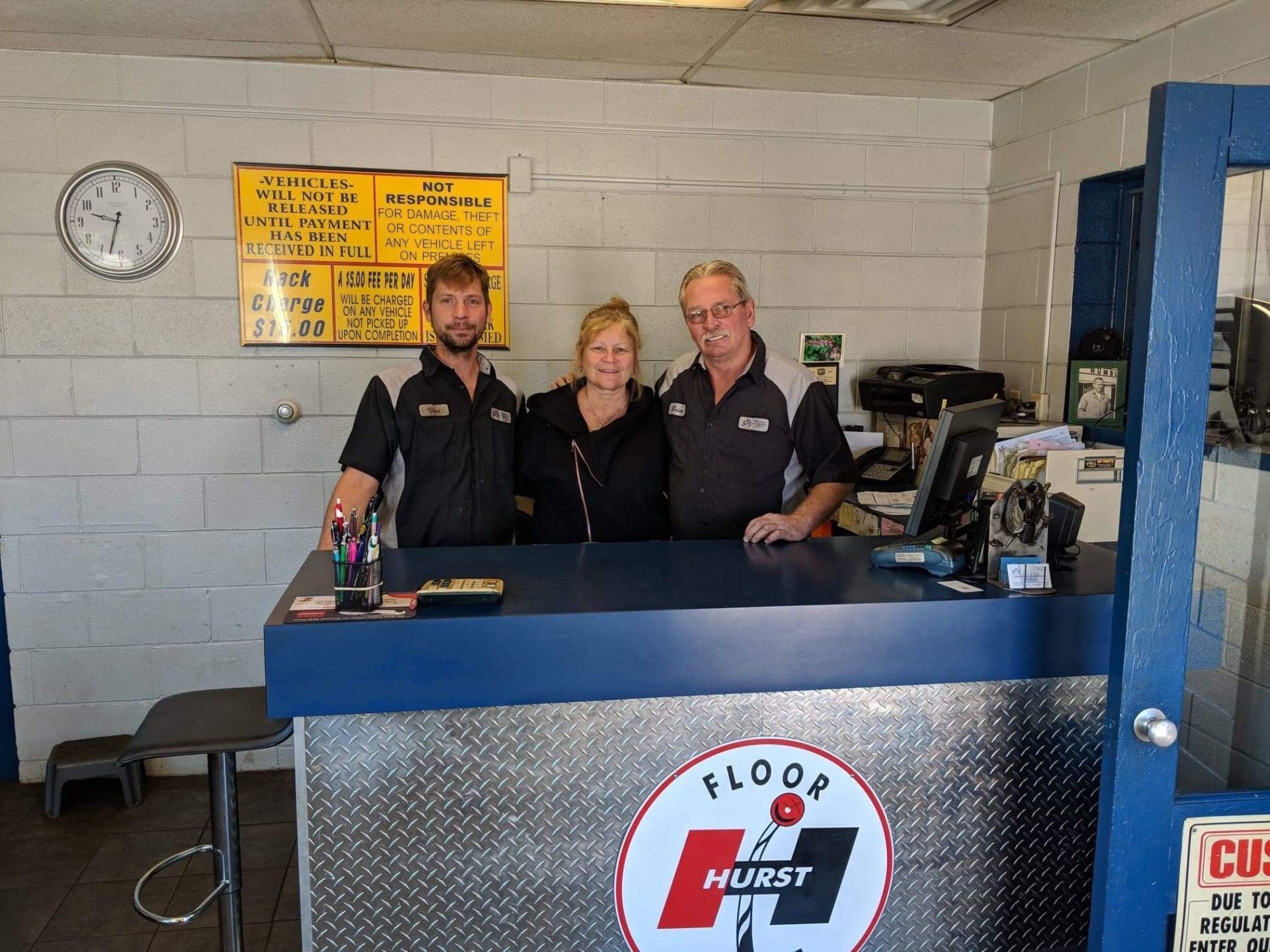 Three people standing behind a blue Hurst service counter in a garage-style workspace