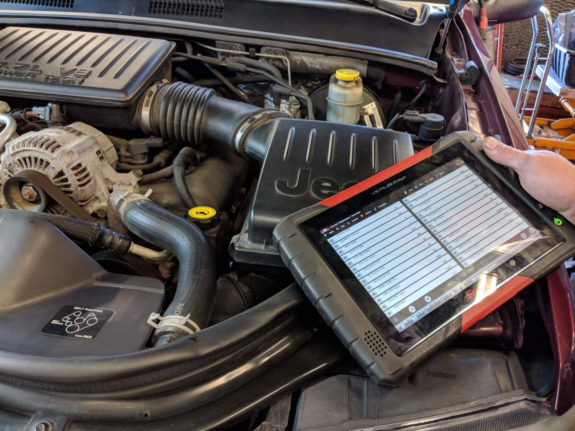Tablet running engine diagnostics beside a car engine in a workshop