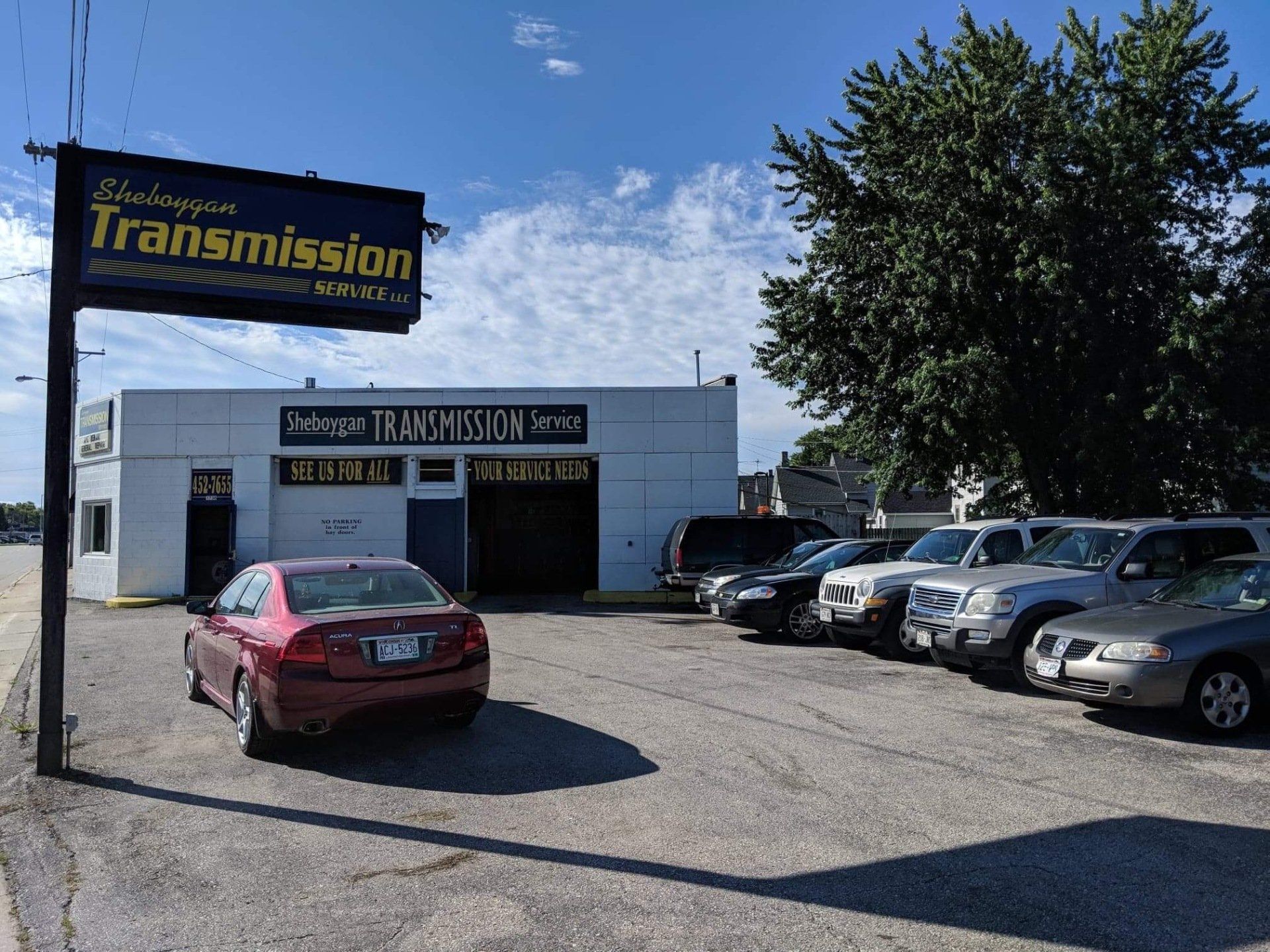 Small transmission shop with parked cars under a blue sky and a large sign out front