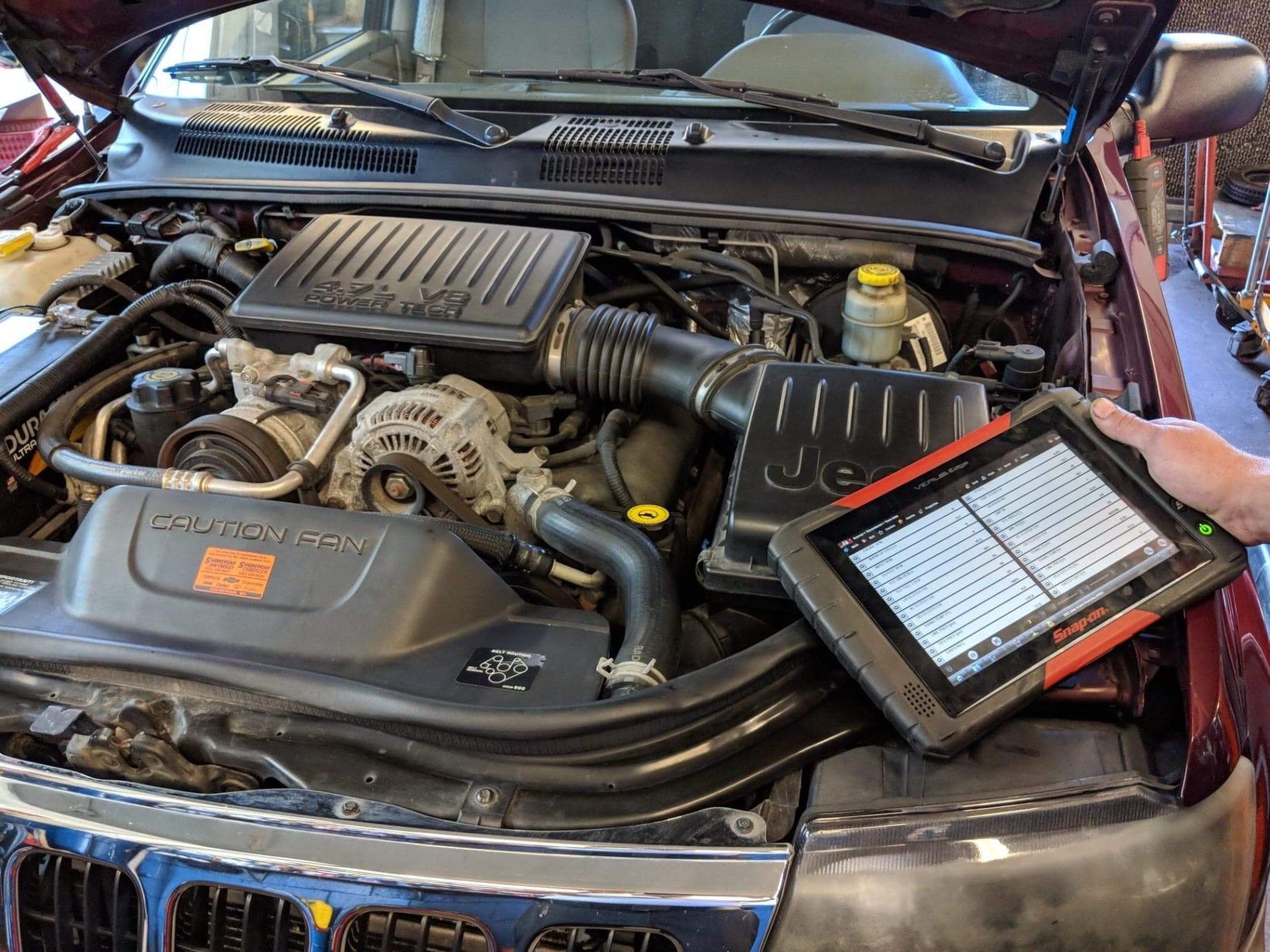Car engine bay with diagnostic tablet resting on the front bumper, hood open in a repair shop