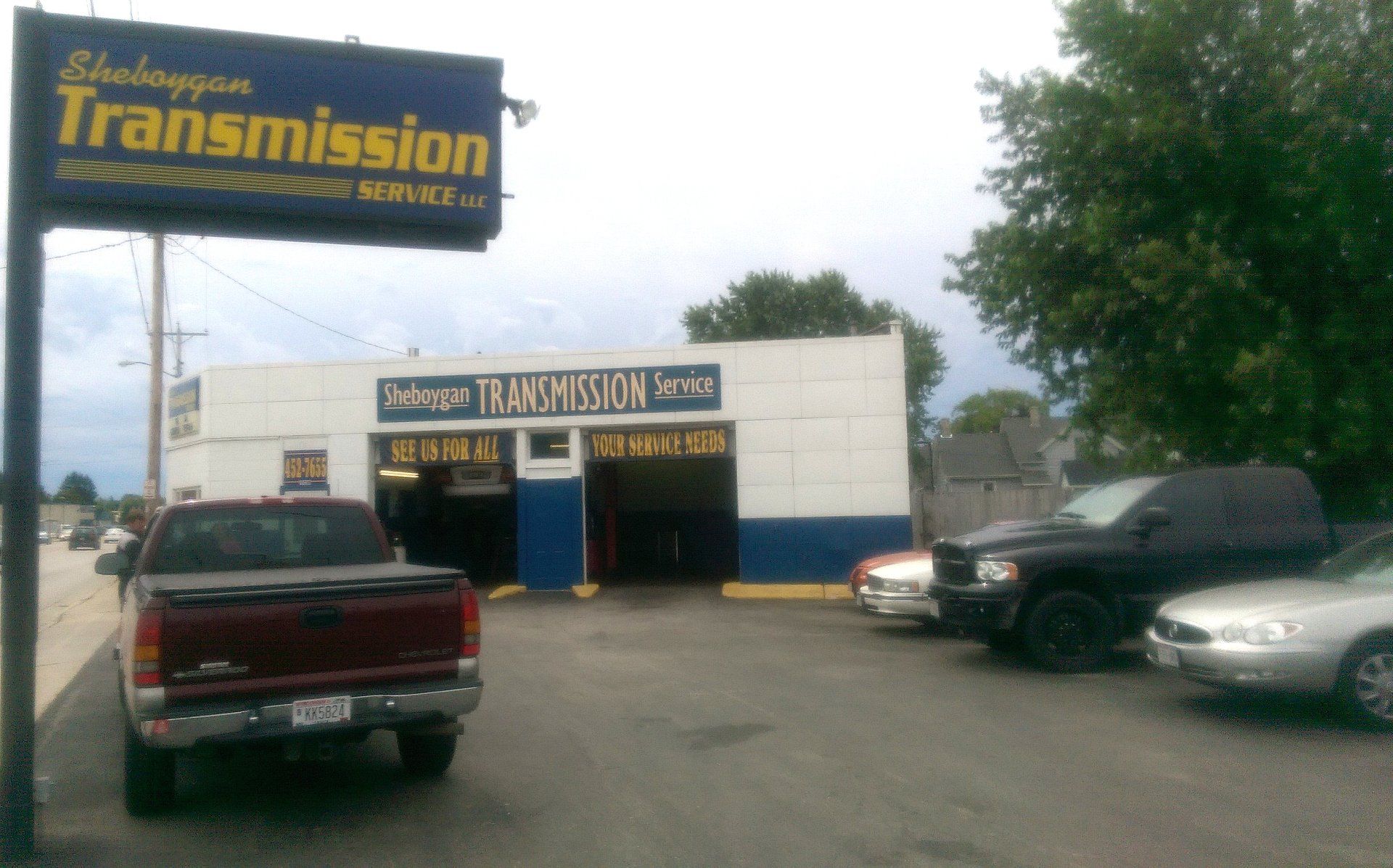 Auto transmission shop with a large sign, parked trucks, and an open garage entrance.