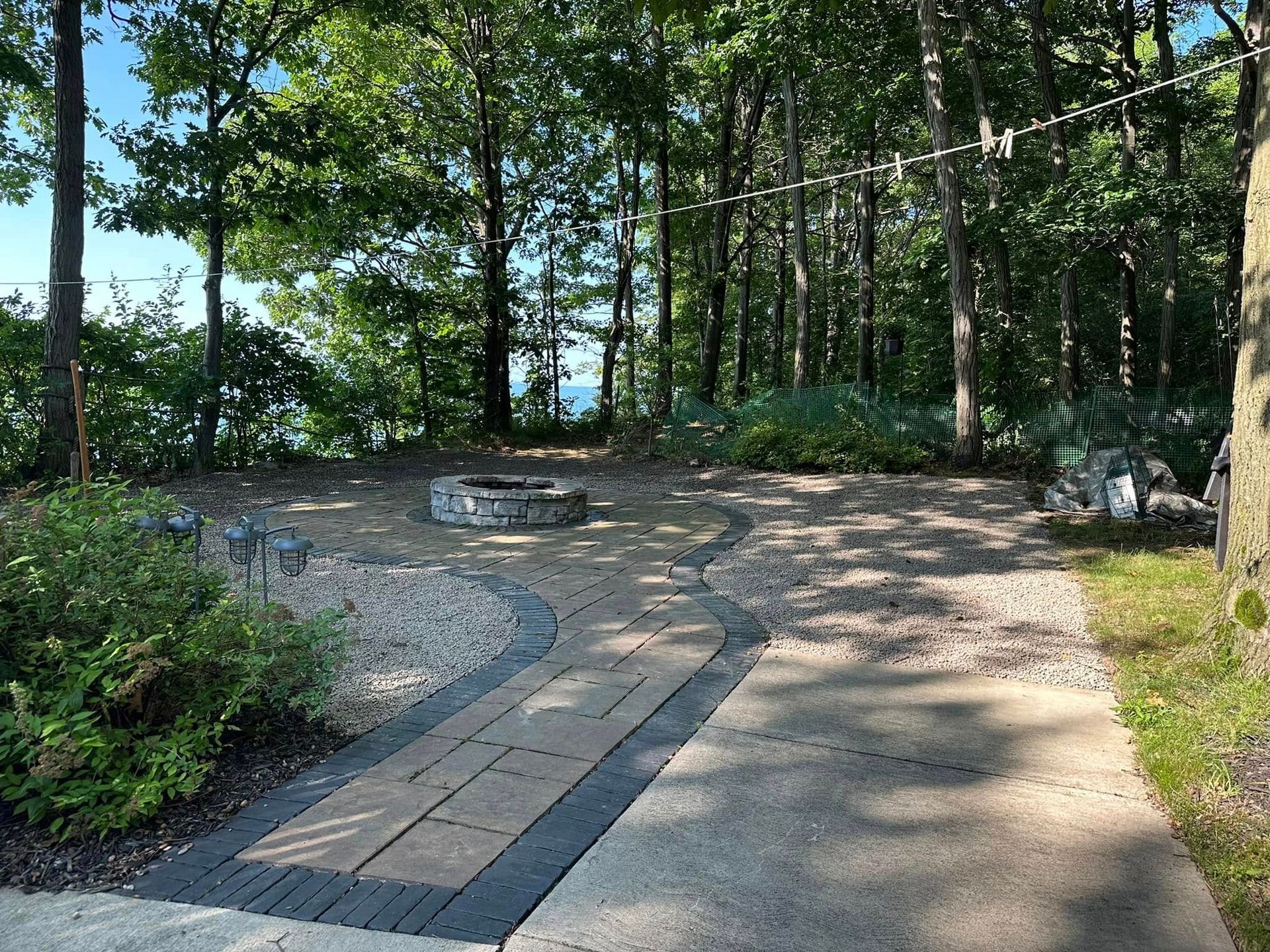 Wooded garden path with a paved walkway, gravel clearing, and trees in bright sunlight