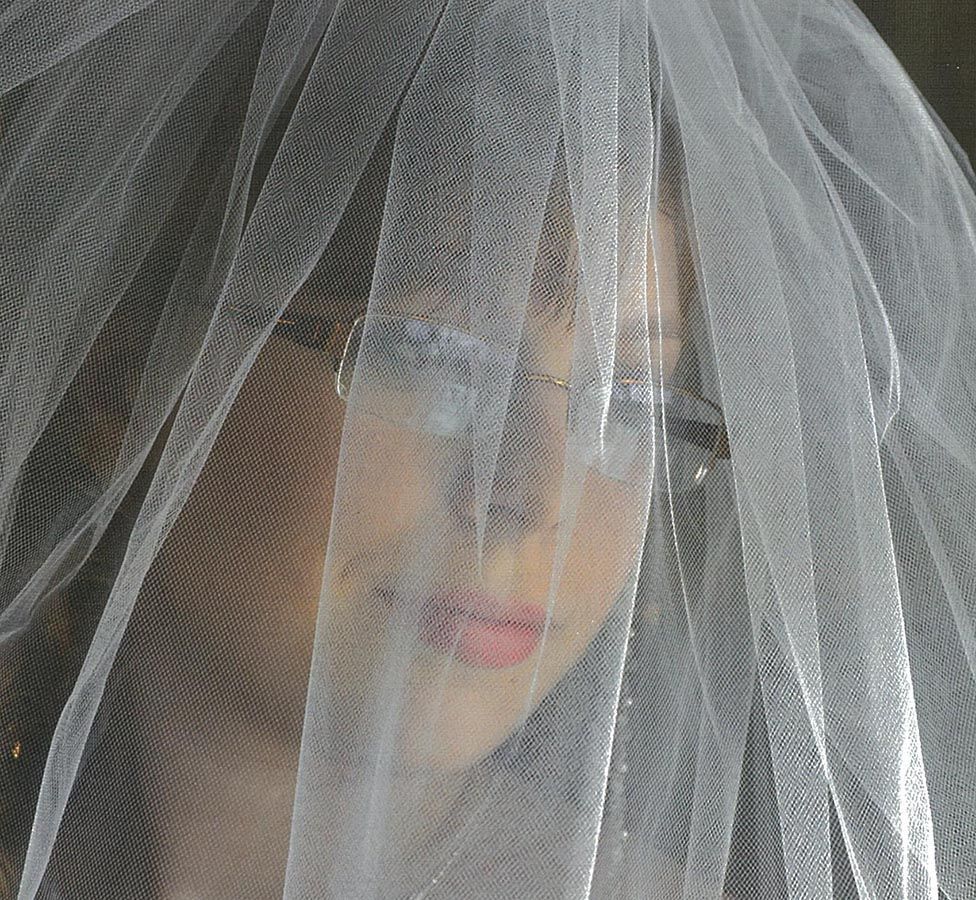A woman is wearing a white veil over her face.