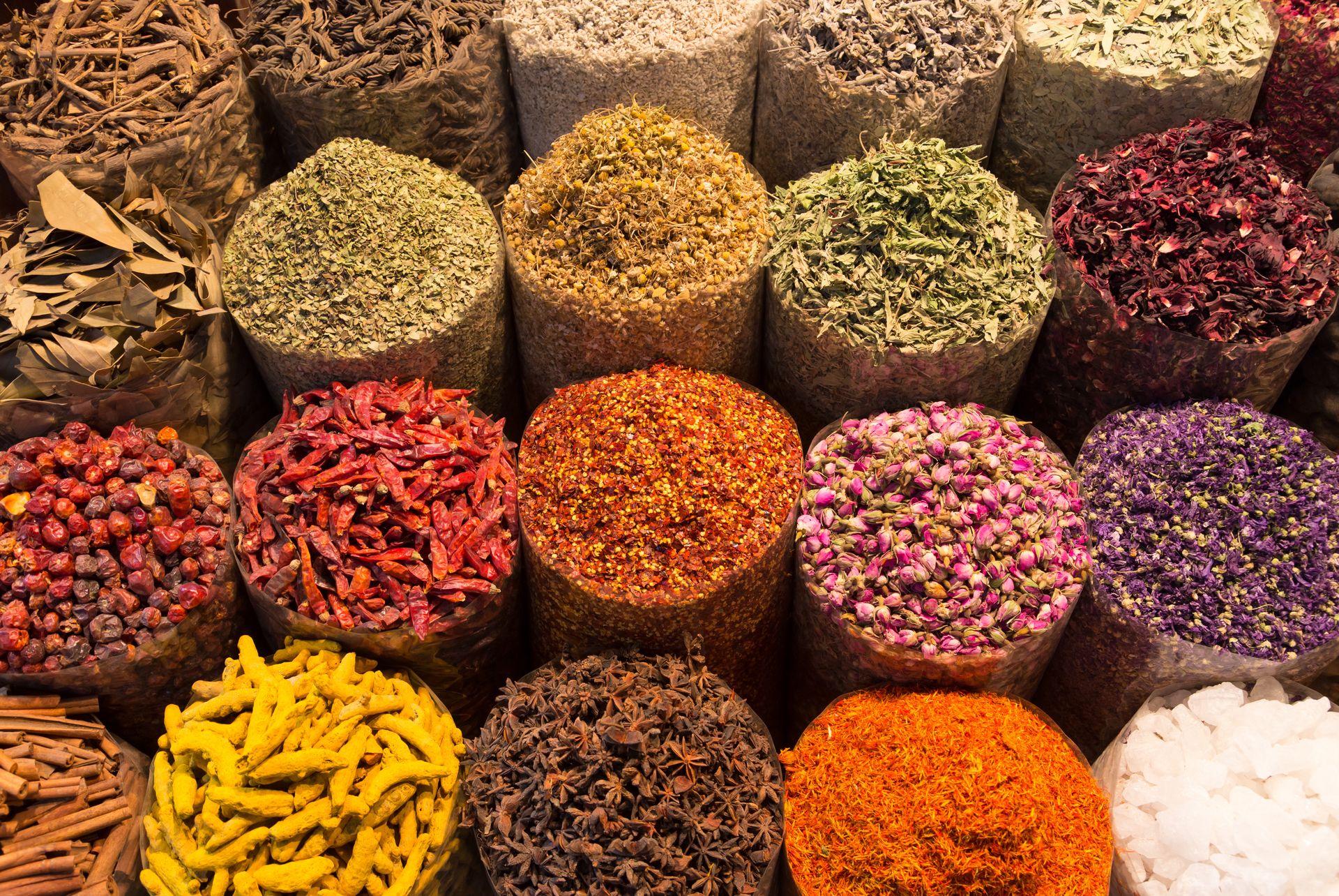 Bags overflowing with a vibrant array of spices; reds, yellows, oranges, greens, and purples in a market.