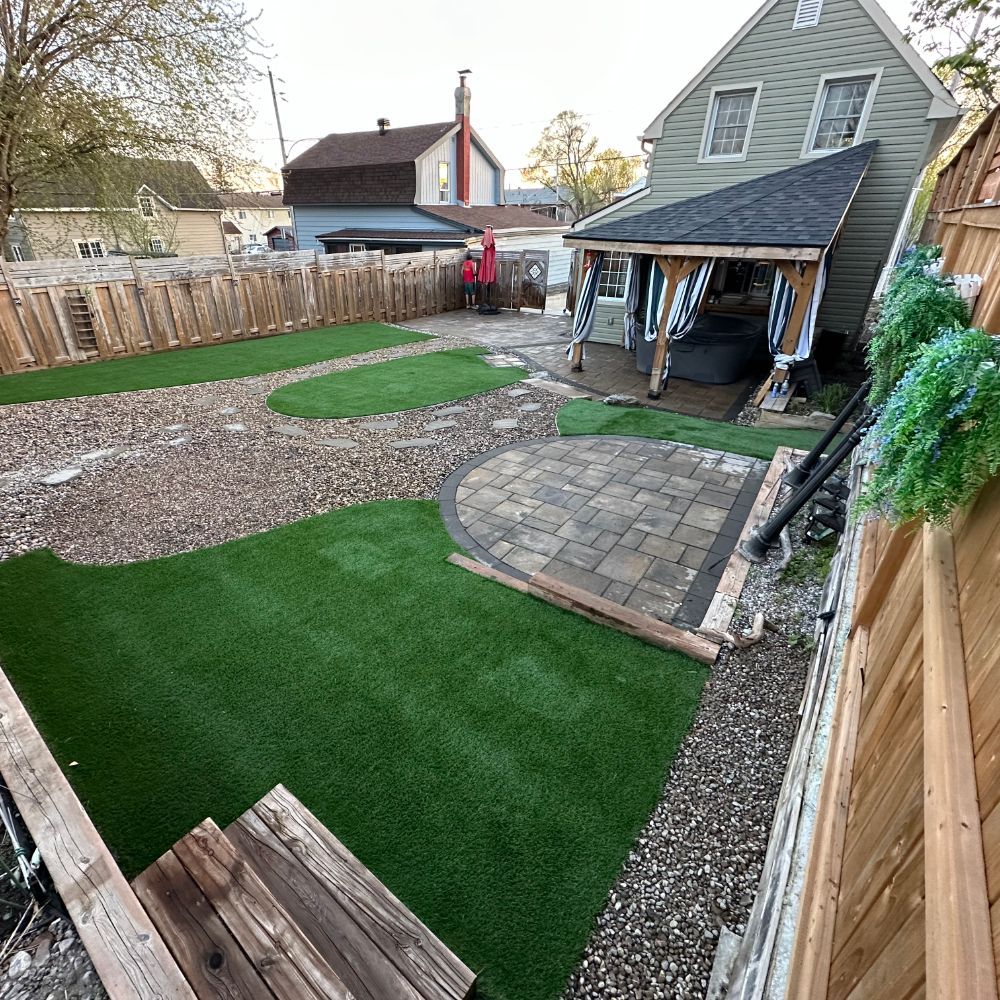 Cour arrière avec gazon artificiel, patio en pierre, clôture en bois et espace spa couvert.