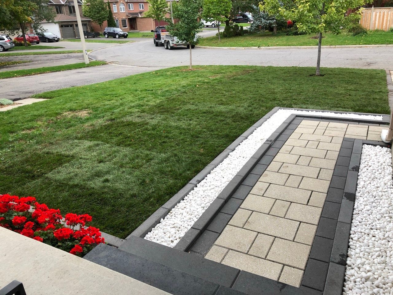 Une cour avant avec une allée en pierre, une pelouse et des fleurs rouges. Du gravier orne les bords de l'allée.