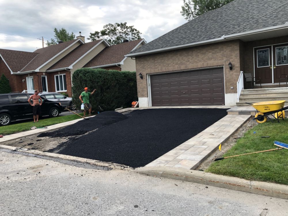 Pavage de l'allée en cours ; deux ouvriers sur le chantier. Un nouvel asphalte noir a été posé à côté d'une bordure en béton clair.