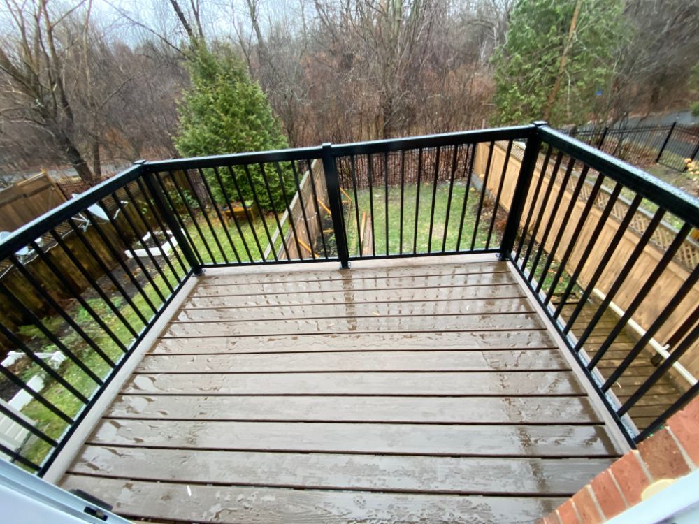 Terrasse en bois avec garde-corps noir, entourée d'arbres.