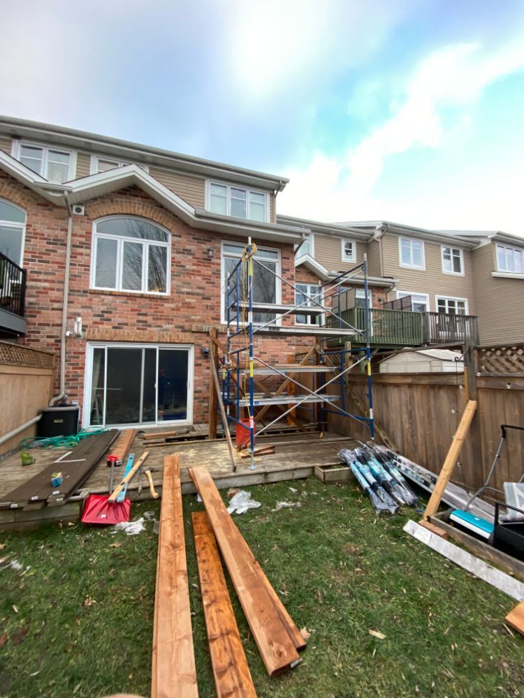 Construction d'une terrasse arrière; échafaudage, construction en briques, planches de bois, herbe verte et ciel nuageux.