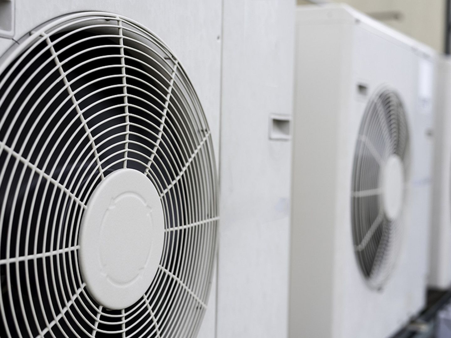 Multiple white outdoor air conditioning condenser units lined up in a row.