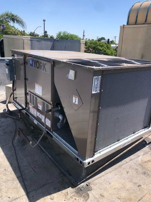A beige York commercial rooftop HVAC unit sits on a flat roof under a clear blue sky.